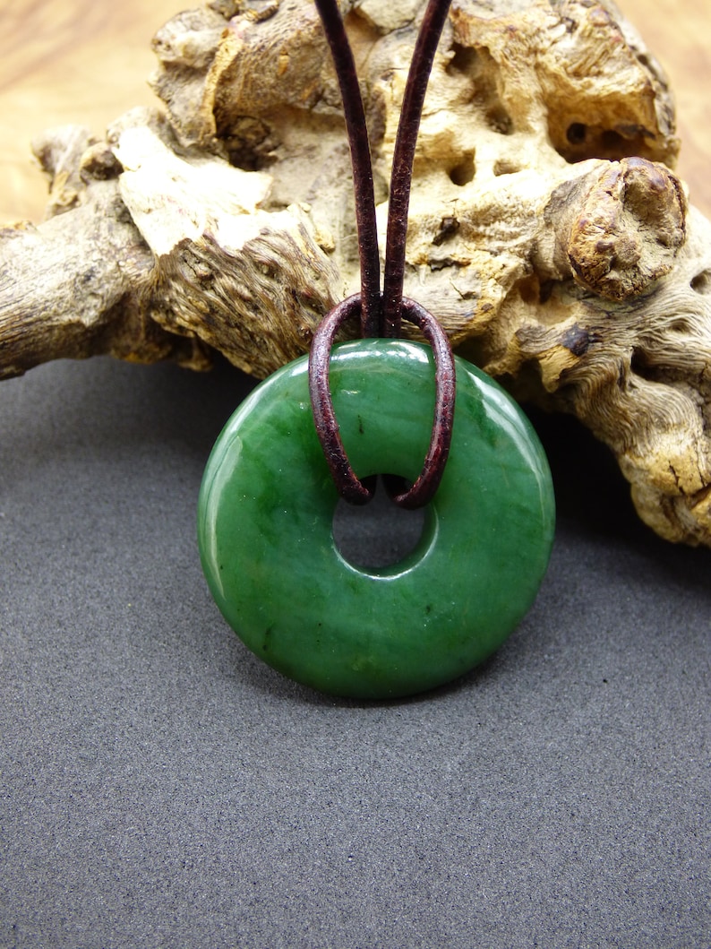 Pu&ograve; includere: Un ciondolo in giada verde a forma di ciambella, con un cordoncino in pelle marrone.