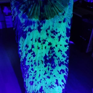 May include: A vibrant, open hand fan with a tie-dye pattern. The fan features a neon green and blue color scheme, with dark blue splotches across the surface. The fan's wooden ribs are visible at the top.