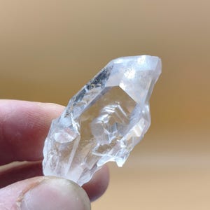 Op de afbeelding: Een heldere, natuurlijk gevormde kwartskristalpunt met een puntige uiteinde en gefacetteerde, onregelmatige oppervlakken. Het mineraalexemplaar vertoont interne insluitingen en een transparant, glasachtig uiterlijk met scherpe randen.