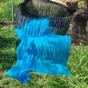 May include: A blue and black silk fabric veil with a rippled texture. The veil is flowing in the wind and is partially obscured by green grass.