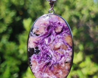 May include: Oval pendant necklace featuring a polished charoite stone with swirling purple, pink, and black patterns. The stone is set in a silver-colored metal frame and hangs from a delicate chain.