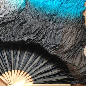 May include: A black and turquoise silk fan with a wooden handle. The fan is folded and has a gradient of color from black to turquoise.