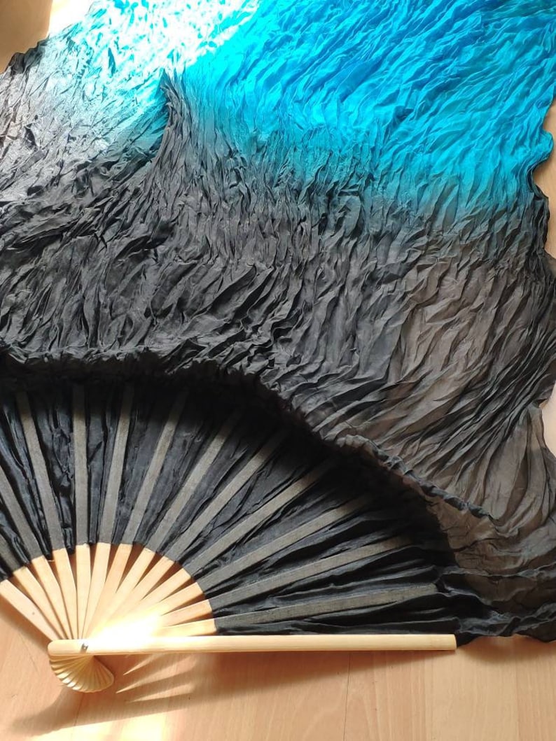 May include: A black and turquoise silk fan with a wooden handle. The fan is folded and has a gradient of color from black to turquoise.