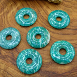 Pode incluir: Seis pedras de aventurina verde em forma de donut com um furo no centro. As pedras est&atilde;o dispostas em c&iacute;rculo sobre uma superf&iacute;cie de madeira.