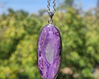 May include: A silver chain necklace with a large oval pendant made of purple and white stone.