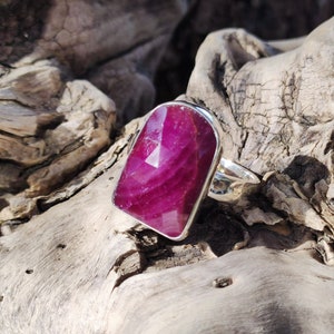 May include: A silver ring with a large, rectangular, faceted ruby gemstone. The ruby is a deep pink color with white streaks.