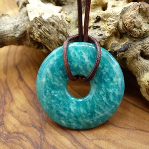 Pode incluir: Um pingente de aventurina verde-azulado em forma de rosquinha com um cord&atilde;o de couro marrom.