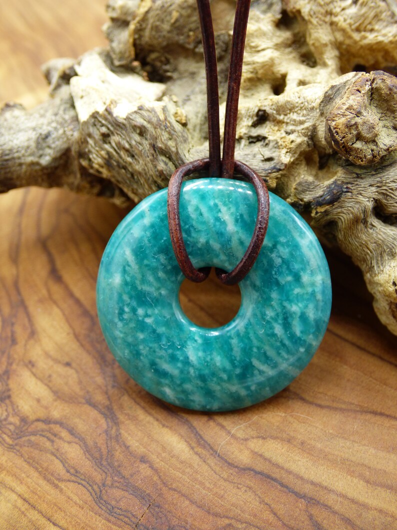 Pode incluir: Um pingente de aventurina verde-azulado em forma de rosquinha com um cord&atilde;o de couro marrom.