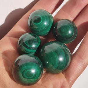 Op de afbeelding: Vijf gladde, groene malachiet bollen met draaiende patronen. De bollen zijn gepolijst en hebben een glanzende afwerking.