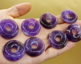 Könnte beinhalten: Sieben amethystfarbene Donut-förmige Perlen mit einem Loch in der Mitte. Die Perlen sind tiefviolett und haben eine glänzende Oberfläche.