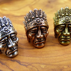 Puede incluir: Tres figuritas de jefe nativo americano, cada una con un acabado metálico diferente: plata, cobre y oro. Cada figurita tiene un tocado con plumas y una banda de cuentas.