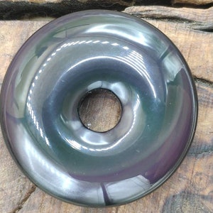 K&ouml;nnte beinhalten: Ein schwarzer Obsidian-Donut mit einem Loch in der Mitte. Der Donut hat eine glatte, polierte Oberfl&auml;che und einen irisierenden Glanz.