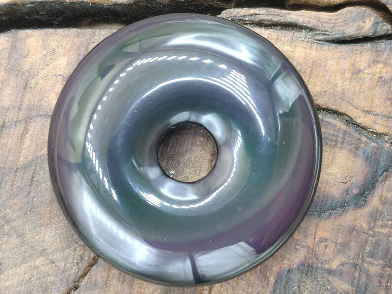 K&ouml;nnte beinhalten: Ein schwarzer Obsidian-Donut mit einem Loch in der Mitte. Der Donut hat eine glatte, polierte Oberfl&auml;che und einen irisierenden Glanz.