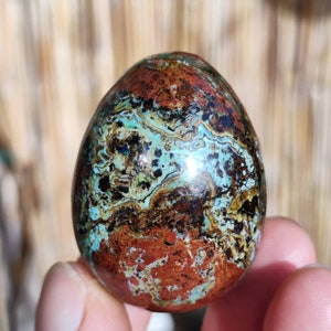 May include: A polished, egg-shaped stone with a swirling pattern of brown, green, and blue. The stone has a smooth, glossy finish.