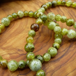 May include: Two green gemstone bracelets with round beads. The beads are a mix of light and dark green with some brown tones.