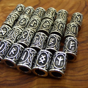 Puede incluir: Un conjunto de 15 cuentas de metal plateadas con intrincados diseños de nudos celtas y runas nórdicas. Cada cuenta presenta un símbolo de runa diferente.