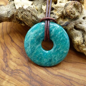 Pode incluir: Um pingente em forma de rosquinha verde-azulado feito de pedra amazonita com um cord&atilde;o de couro marrom.
