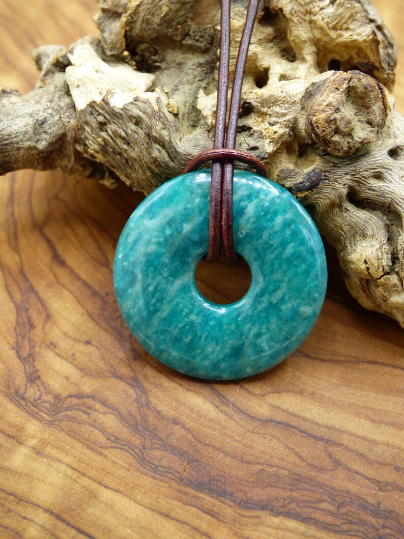 Pode incluir: Um pingente em forma de rosquinha verde-azulado feito de pedra amazonita com um cord&atilde;o de couro marrom.