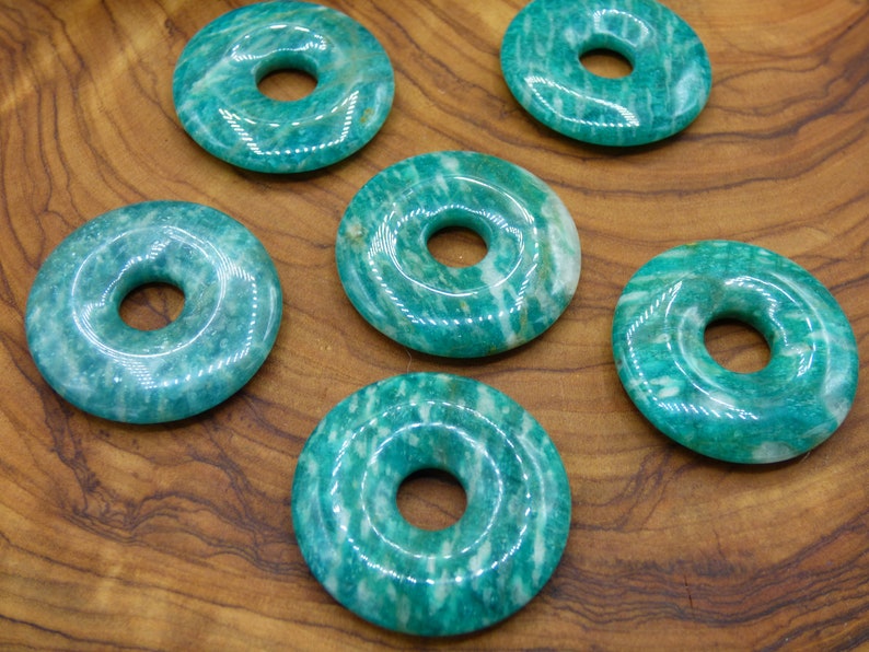 Pode incluir: Seis pedras de aventurina verde em forma de donut com um furo no centro. As pedras est&atilde;o sobre uma superf&iacute;cie de madeira.