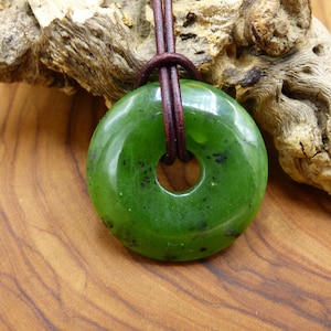 Könnte beinhalten: Ein grüner Jade-Anhänger in Ringform mit einem braunen Lederband.