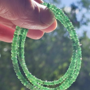 Könnte beinhalten: Eine Kette aus grünen Edelsteinperlen, wahrscheinlich Smaragde, die auf einem dünnen Draht aufgefädelt sind. Die Perlen sind klein und gleichmäßig groß, was einen zarten und eleganten Look erzeugt.