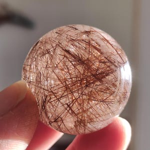 Op de afbeelding: Een heldere kwartsbol met een hoge concentratie rode rutiel-insluitsels. De bol heeft een diameter van ongeveer 5 cm en een glad, gepolijst oppervlak.
