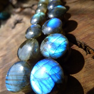 Puede incluir: Una hebra de cuentas de piedra preciosa de labradorita azul iridiscente. Las cuentas son redondas y lisas, con un brillo brillante, casi metálico.