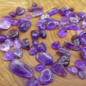 Op de afbeelding: Een verzameling amethist-tumbled stones in verschillende maten en vormen. De stenen zijn diep paars van kleur en hebben een gladde, gepolijste afwerking.