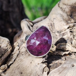 Può includere: Un anello d'argento con una grande pietra preziosa viola sfaccettata a forma di lacrima.