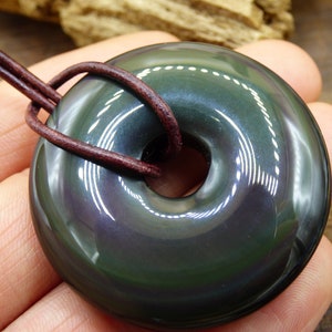 K&ouml;nnte beinhalten: Ein dunkler gr&uuml;ner Obsidian-Donut-Anh&auml;nger mit einem Lederband. Der Anh&auml;nger hat einen hohen Glanz und einen irisierenden Schimmer.