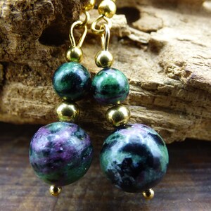 May include: A pair of gold earrings with green and black gemstone beads. The beads are round and have a mottled appearance.