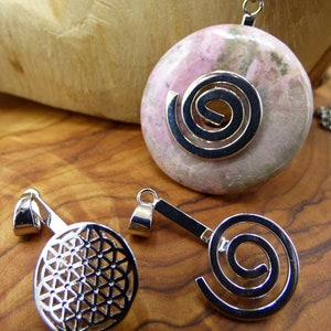 Peut inclure: Trois breloques de pendentif argentées avec des motifs différents. Un charme présente une pierre rose et grise avec un motif en spirale argentée. Un autre charme présente un motif argenté de la fleur de vie. Le troisième charme présente un motif en spirale argenté.