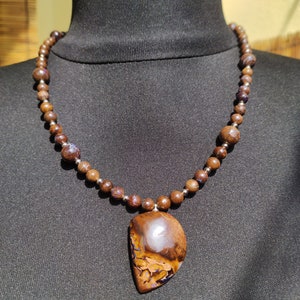 Könnte beinhalten: Eine Halskette mit einem Anhänger aus braunem und violettem Opal an einer Kette aus braunen Holzperlen.