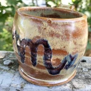 May include: A brown and yellow ceramic mug with a black and blue design. The mug has a rounded shape and a wide base.