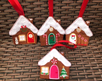 Peut inclure: Quatre décorations de maison en pain d'épices avec des rubans rouges. Chaque maison a un toit blanc avec un motif différent sur le devant. Les motifs comprennent un bonhomme de neige, des cannes en sucre, un cœur et une canne en sucre et un sapin de Noël.