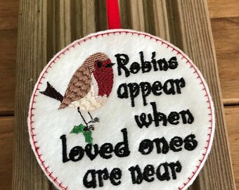 May include: A white felt ornament with red stitching, featuring an embroidered robin and the text "Robins appear when loved ones are near".