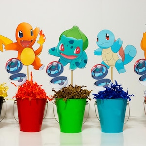May include: Seven colorful plastic buckets with paper cutouts of Pokemon characters, including Pikachu, Bulbasaur, Charmander, Squirtle, and a brown Pokemon with a large nose. Each bucket is filled with colorful shredded paper.