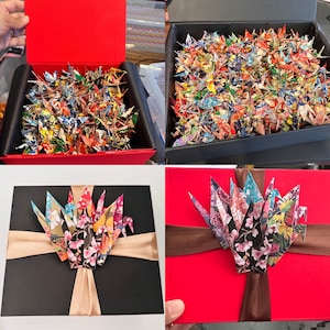 May include: Three gift boxes with origami paper cranes. The first box is red with a lid and is filled with colorful paper cranes. The second box is black with a gold ribbon and has a floral design on the cranes. The third box is red with a brown ribbon and has floral design cranes.