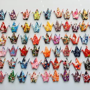 May include: A wall display of colorful origami cranes made from patterned paper. The cranes are arranged in rows and columns, creating a visually appealing and intricate design.