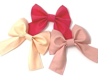 Peut inclure: Trois nœuds en tissu pour cheveux dans différentes nuances de rose. Les nœuds sont noués en forme de nœud classique et sont prêts à être portés dans les cheveux.