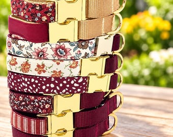 May include: A stack of eight pet collars featuring various patterns and solid colors in shades of red, burgundy, and cream. Each collar is equipped with a shiny gold-toned metal side-release buckle and a matching gold-toned D-ring for leash attachment.