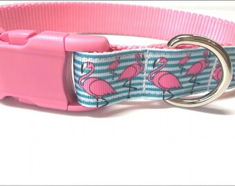 May include: Pink dog collar with a flamingo pattern. The collar features a pink plastic buckle and a silver metal D-ring. The flamingo pattern is on a blue and white striped background.