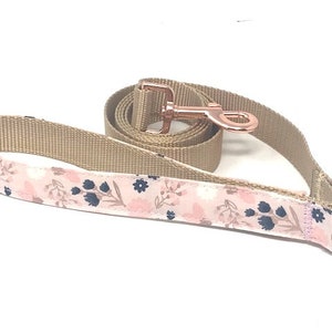 May include: A pink and brown dog lead with a floral pattern and a rose gold metal clip.
