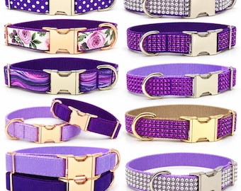 May include: A collection of ten pet collars in various shades of purple, featuring gold-toned metal buckles and D-rings. Designs include polka dots, floral patterns, marbled swirls, solid colors, and rhinestone-encrusted textures.