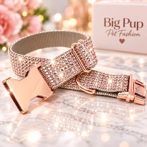 May include: A pet collar covered in light pink rhinestones with a rose gold metal buckle and hardware. The collar features a side-release clasp and a D-ring. A white box in the background displays the text Big Pup Pet Fashion with a heart icon.