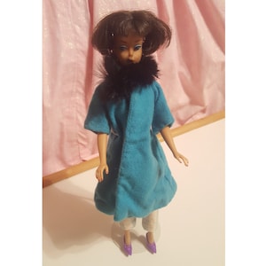 May include: A vintage doll with brown hair wearing a teal blue coat with a black fur collar and purple shoes.