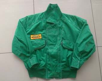 May include: A green jacket with white stitching and a yellow patch that says "Benetton Formula One Marlboro World Championship".