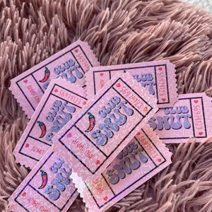 May include: Pink glittery tickets with the text "Club Shut" and a chili pepper graphic. Each ticket has a unique number and the words "Admit One". The tickets are scattered on a fluffy, pink surface.
