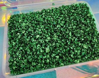 May include: A clear plastic container filled with small, green, glittery, irregular shaped stones.