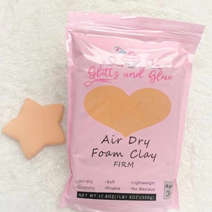 May include: A pink bag of "Glittz and Glue" air dry foam clay with a peach-colored heart design. The bag also features the text "Air Dry Foam Clay FIRM" and a peach-colored star-shaped foam clay. The net weight is 17.6 oz.